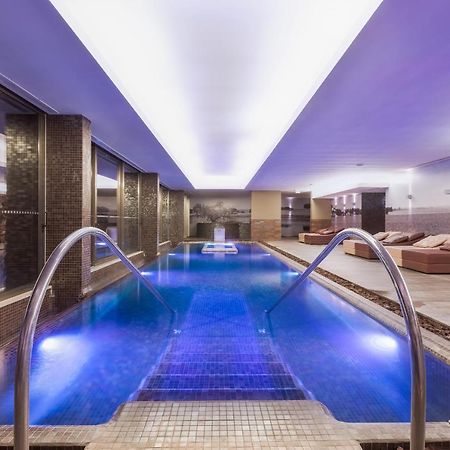 Ap Lago Montargil - Conference & Spa Ngoại thất bức ảnh The photo shows a modern indoor swimming pool area. The pool features a sleek design with steps leading into the water and a gentle curve at the sides. The water is illuminated in a blue hue, enhancing the relaxing atmosphere. Surrounding the pool ar