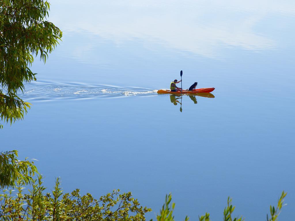Ap Lago Montargil - Conference & Spa Ngoại thất bức ảnh The photo shows a serene scene of a person kayaking on a calm body of water. The surface of the water is very smooth, reflecting the surroundings, and there is a gentle wake behind the kayak indicating movement. The kayaker is wearing a life jacket a