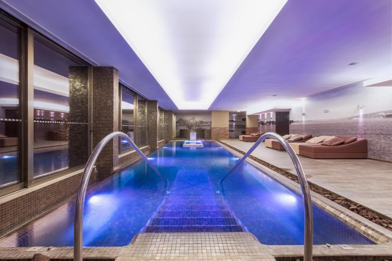 Ap Lago Montargil - Conference & Spa Ngoại thất bức ảnh The photo shows a modern indoor swimming pool area. The pool features a sleek design with steps leading into the water and a gentle curve at the sides. The water is illuminated in a blue hue, enhancing the relaxing atmosphere. Surrounding the pool ar