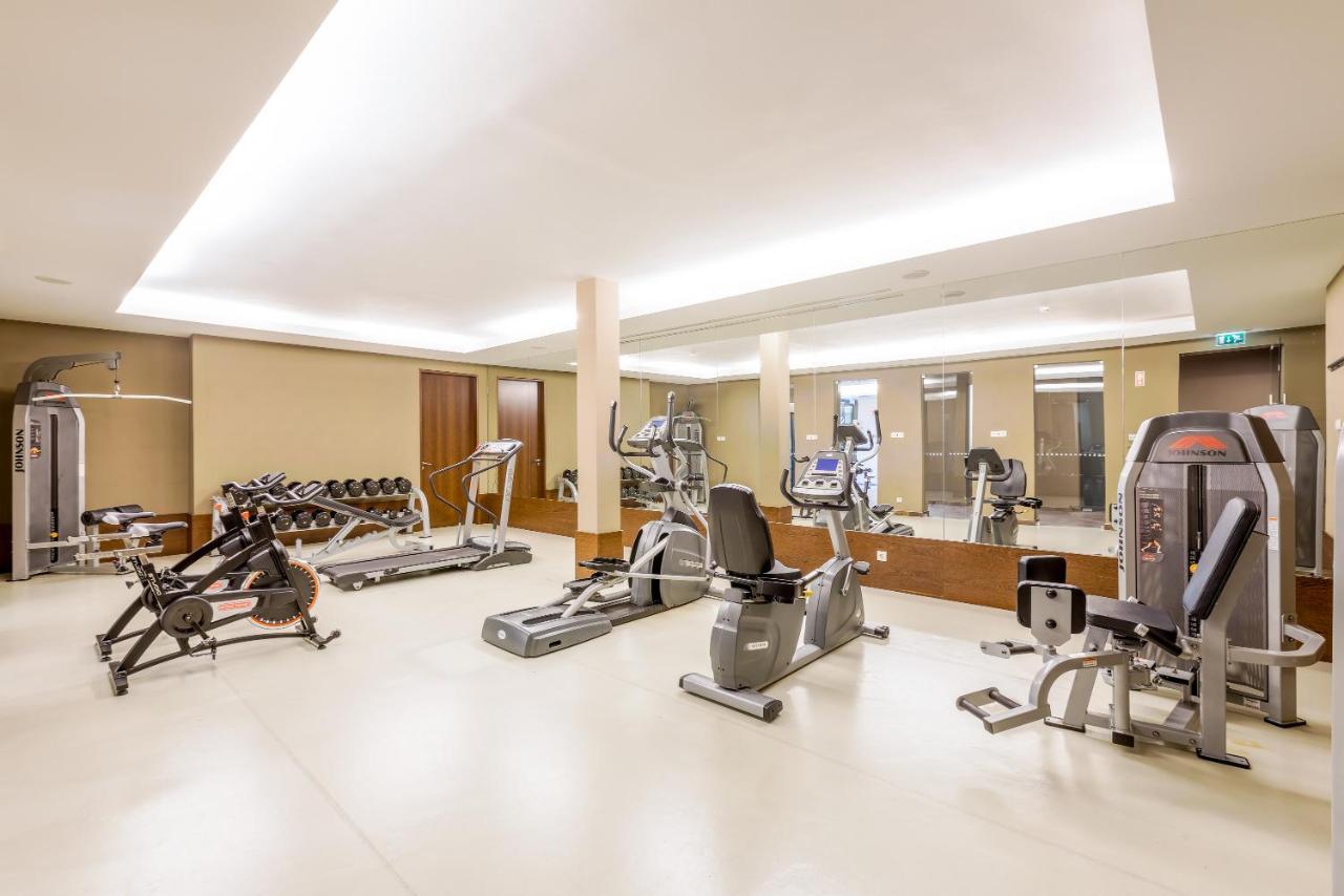 Ap Lago Montargil - Conference & Spa Ngoại thất bức ảnh The image shows a modern gym interior featuring various exercise equipment. On the left, there are free weights and weight benches. In the center, there are multiple machines, including a stationary bike and an elliptical. The space is well-lit with 