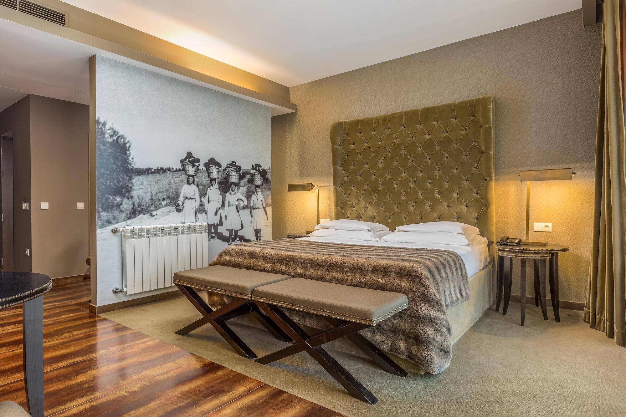 Ap Lago Montargil - Conference & Spa Ngoại thất bức ảnh The photo shows a modern hotel room with a large, plush bed that has a tufted, green headboard. The bedding is white with a textured blanket at the foot of the bed. A decorative wall behind the bed features a black and white mural of children in a fi