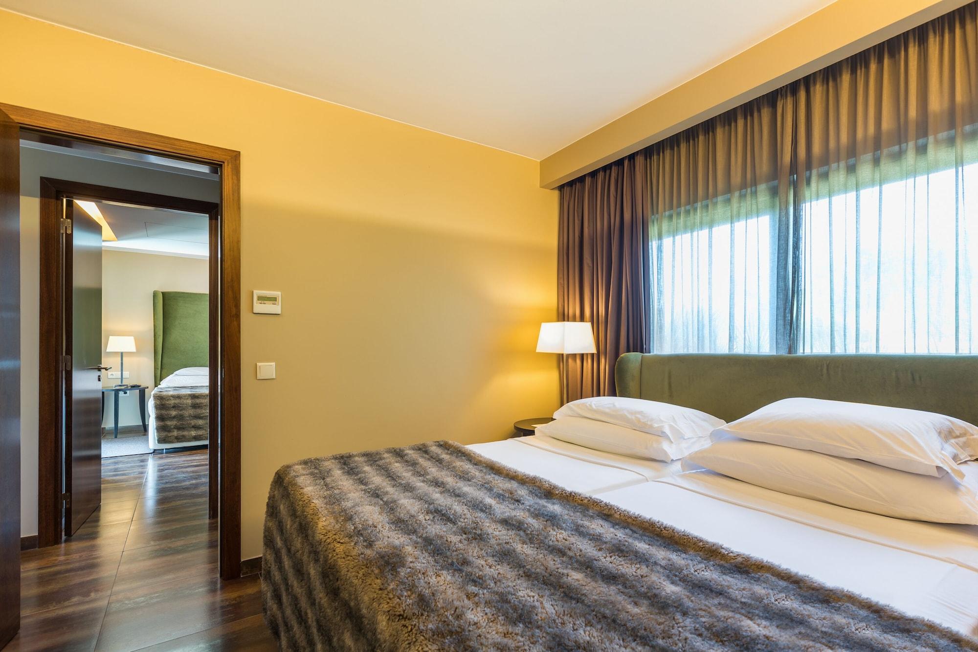 Ap Lago Montargil - Conference & Spa Ngoại thất bức ảnh The photo shows the interior of a well-furnished hotel room. It features two beds with white linens and a gray decorative throw on top. The walls are painted a warm yellow, and there are floor-to-ceiling windows covered with dark curtains that allow 
