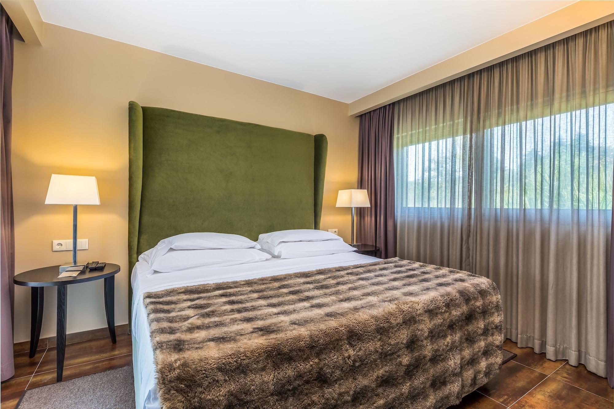 Ap Lago Montargil - Conference & Spa Ngoại thất bức ảnh The photo shows a cozy hotel room featuring a large bed with two white pillows and a fur-style blanket draped over it. Behind the bed is a tall, green headboard that adds a touch of color to the room. On either side of the bed are bedside tables, eac
