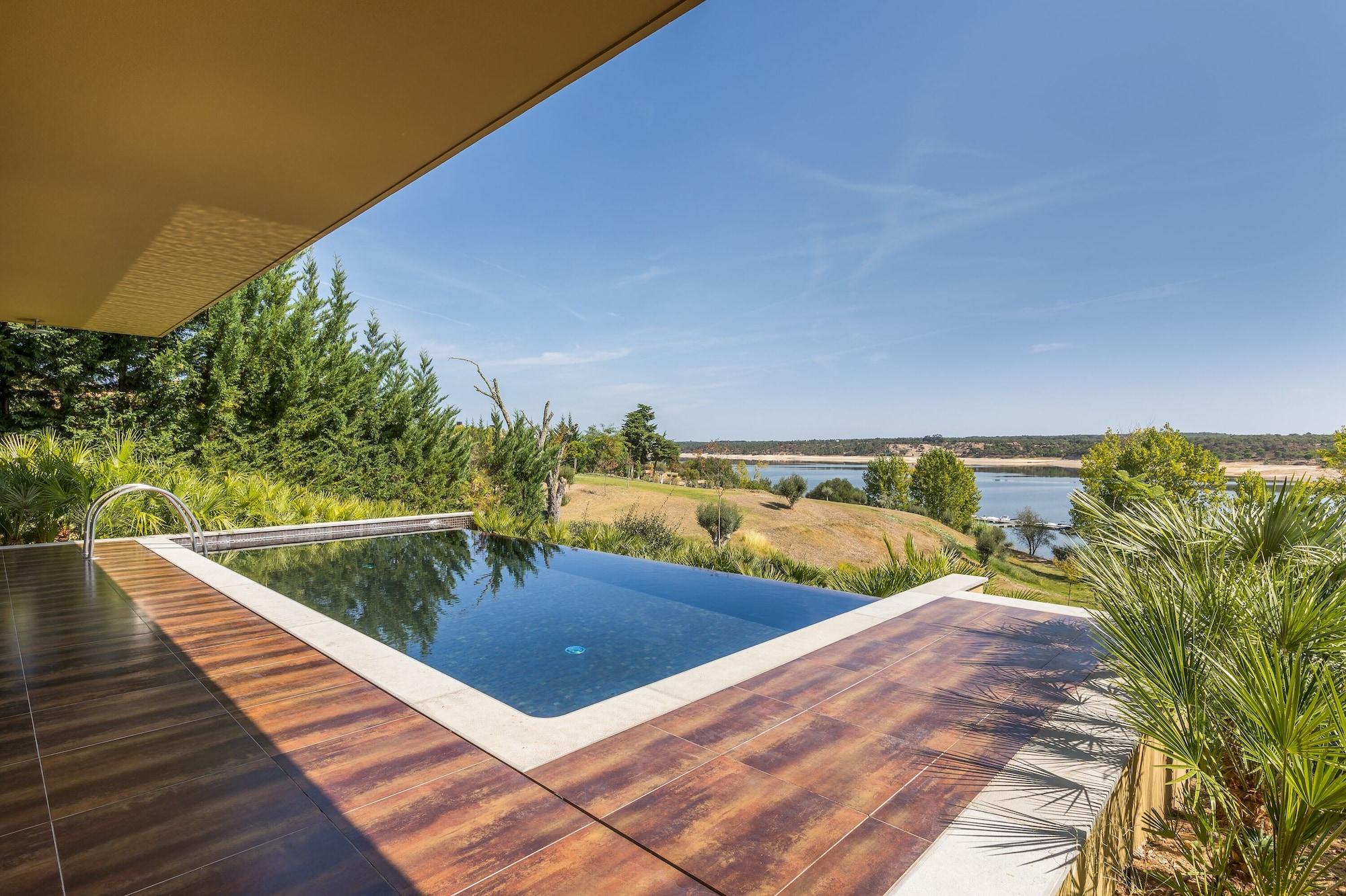 Ap Lago Montargil - Conference & Spa Ngoại thất bức ảnh The photo shows a luxurious infinity pool situated on a terrace or deck. The pool features a sleek, modern design with a dark blue surface that reflects the surrounding scenery. In the background, there is a landscape of rolling hills and a body of w