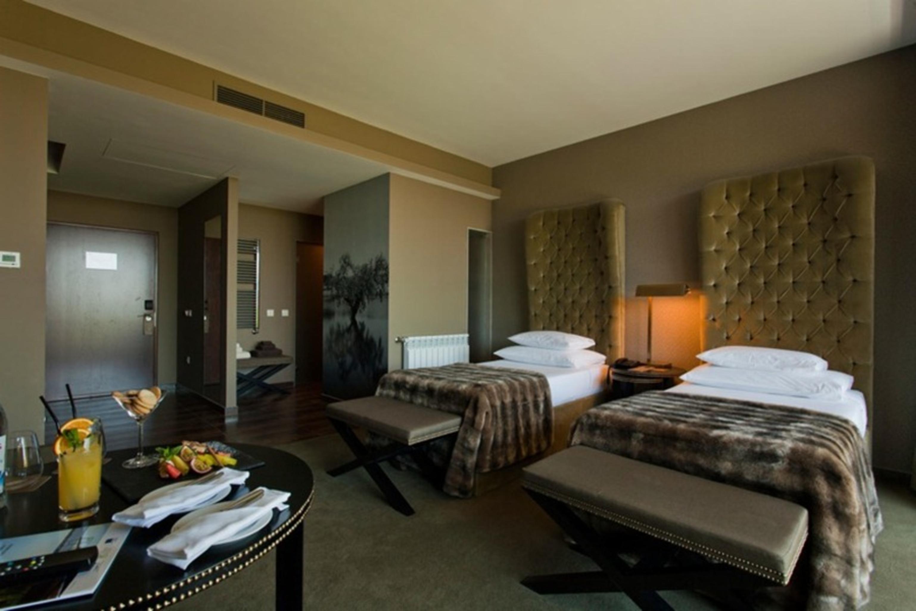 Ap Lago Montargil - Conference & Spa Ngoại thất bức ảnh The photo shows a stylish hotel room featuring two beds with plush, upholstered headboards. The room has a modern and elegant design, with earthy tones dominating the decor. A small round table is set up in the foreground, displaying a drink and some