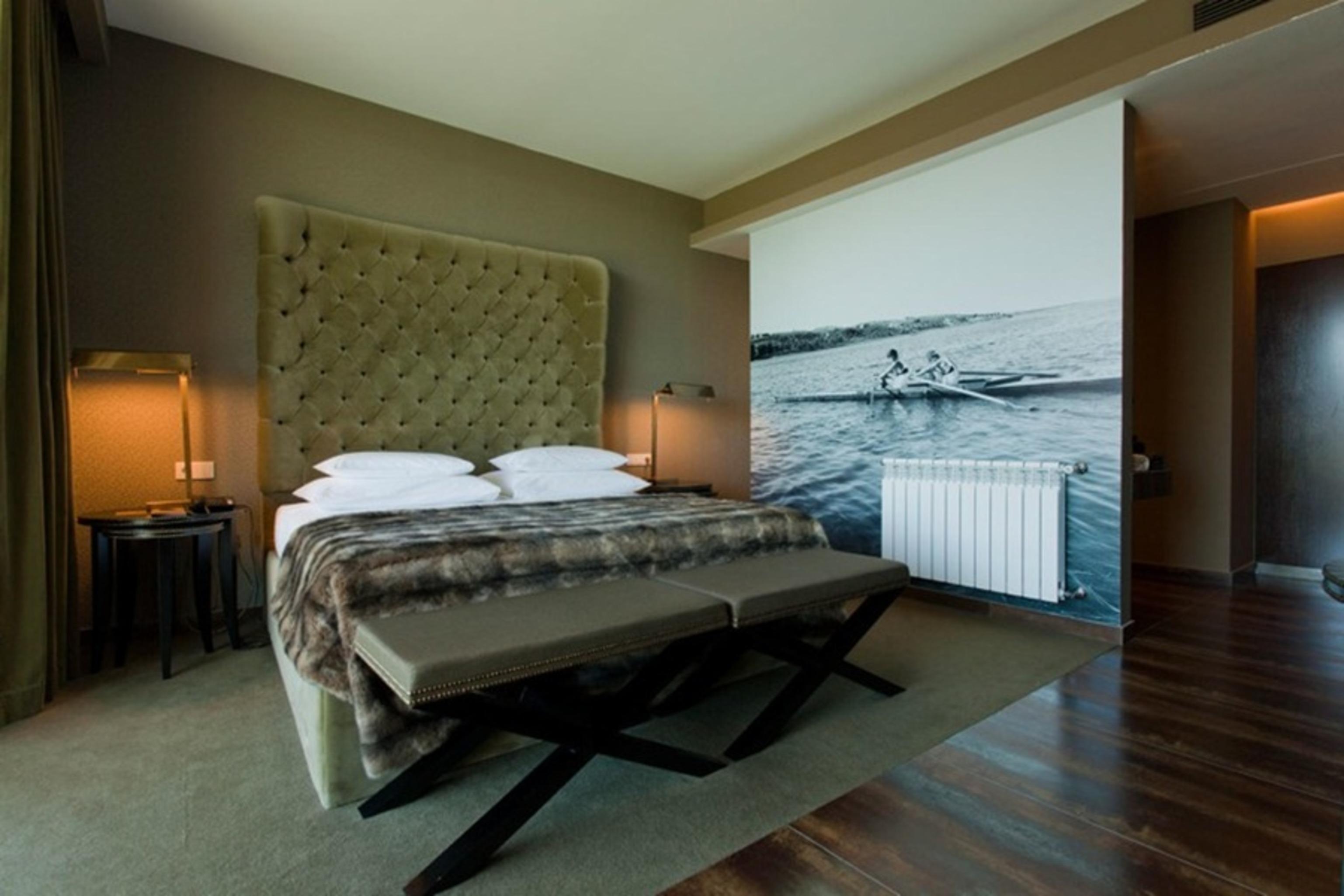 Ap Lago Montargil - Conference & Spa Ngoại thất bức ảnh The photo shows a modern hotel room featuring a large bed with a tufted headboard and plush bedding. The color palette is neutral, with shades of green and gray. On one side of the room, there are bedside tables with lamps. A comfortable bench sits a
