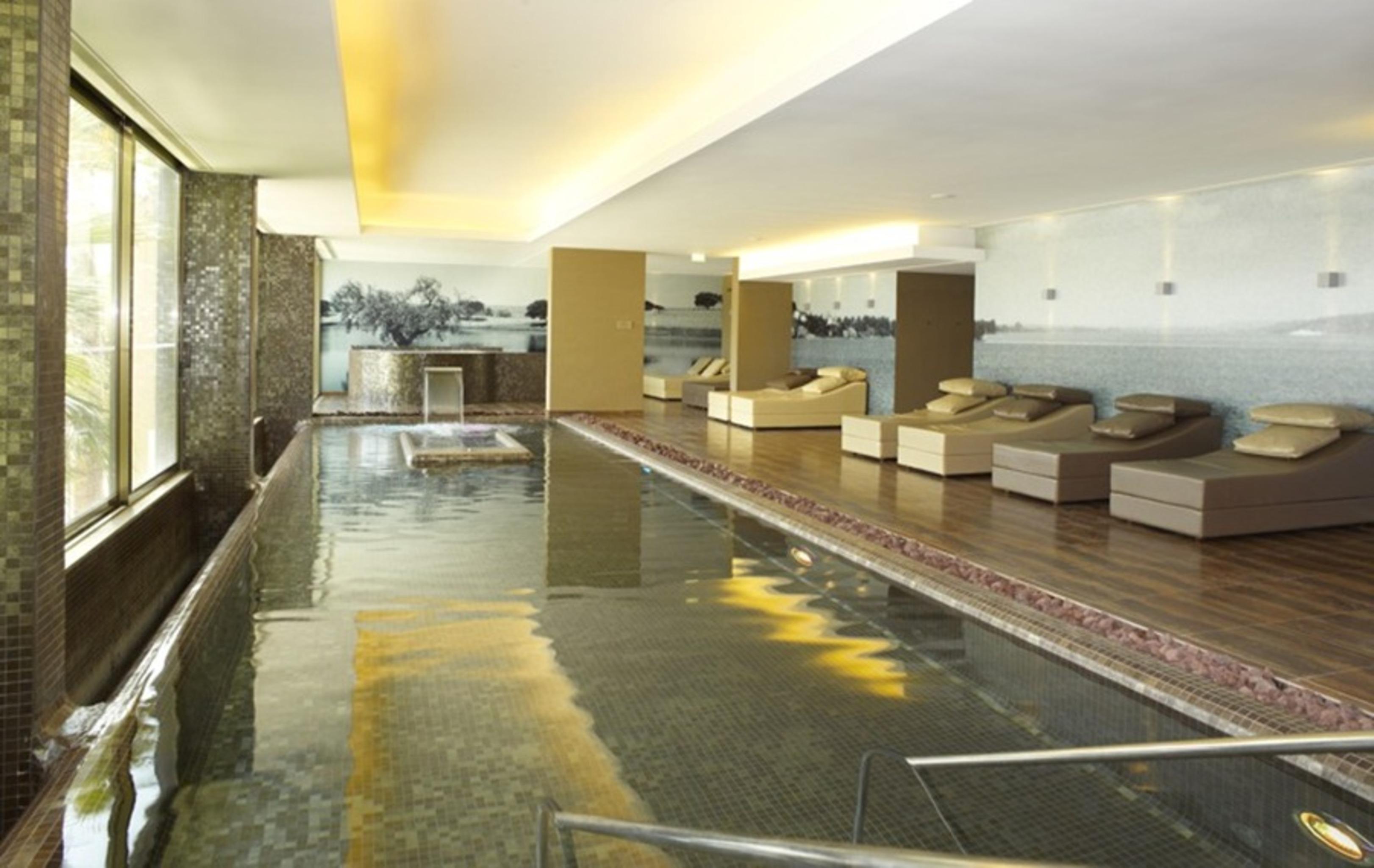 Ap Lago Montargil - Conference & Spa Ngoại thất bức ảnh The photo shows a modern, serene spa environment. There is a swimming pool with calm water, reflecting the surrounding decor. Along the sides, there are several comfortable lounge chairs arranged, perfect for relaxation. Large windows allow natural l