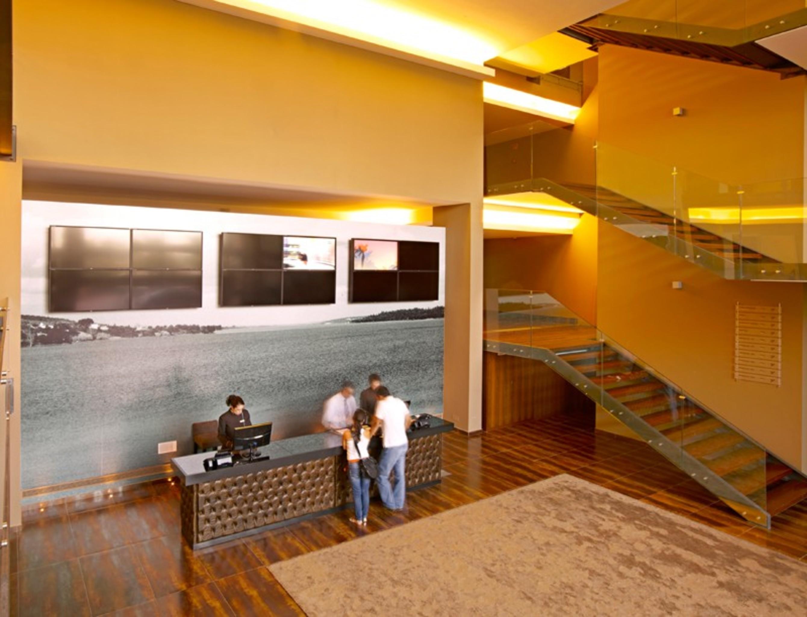 Ap Lago Montargil - Conference & Spa Ngoại thất bức ảnh The photo depicts a modern lobby area with a reception desk. The design features a combination of warm colors and wood flooring. In the background, there is a large wall-mounted screen or display, showcasing several monitors. The wall behind the desk