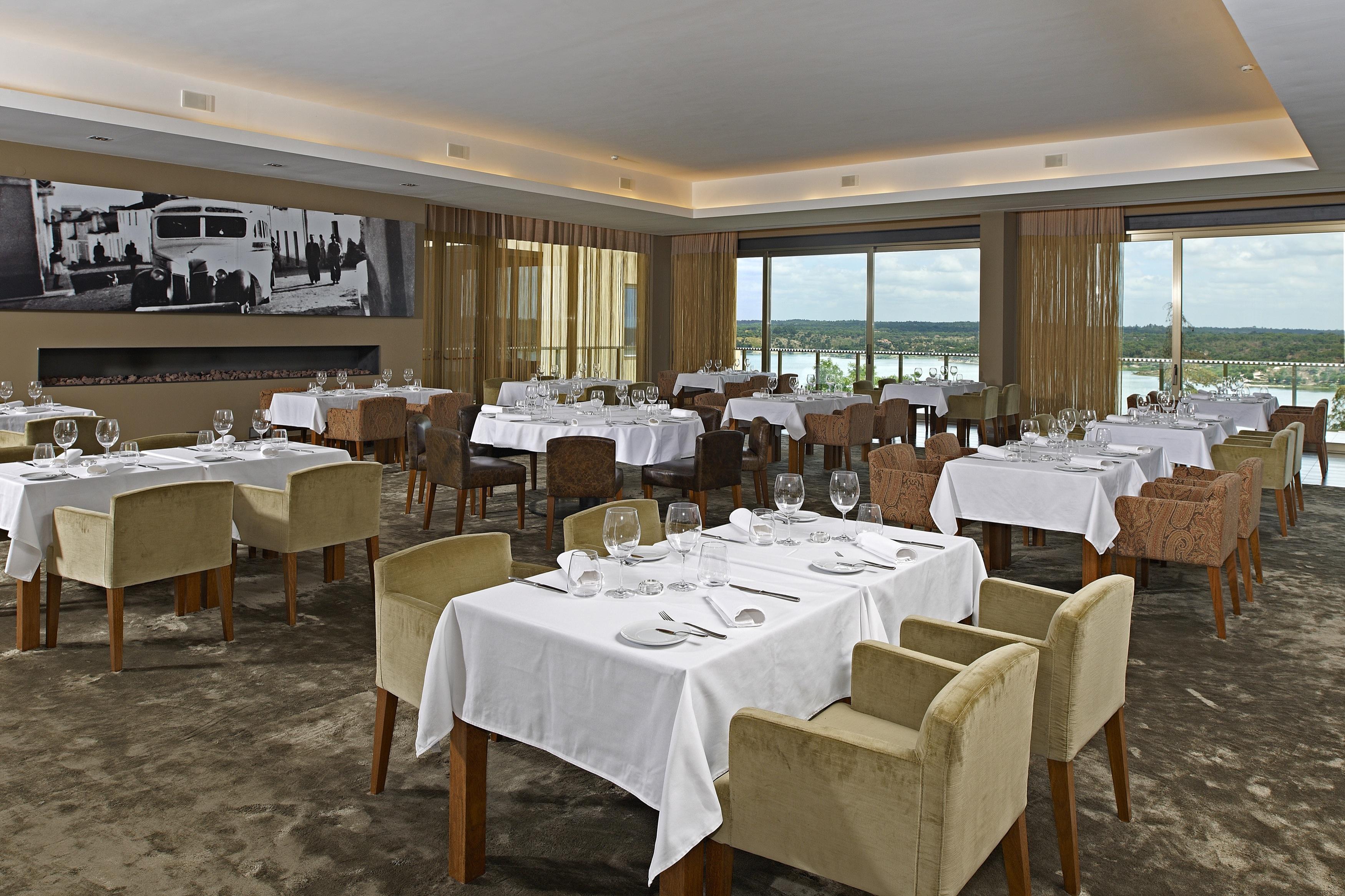 Ap Lago Montargil - Conference & Spa Ngoại thất bức ảnh The photo shows an elegant restaurant interior featuring neatly arranged tables with white tablecloths. Each table is set with plates, cutlery, and glasses. The seating includes a mix of upholstered chairs in different colors—some light and others da