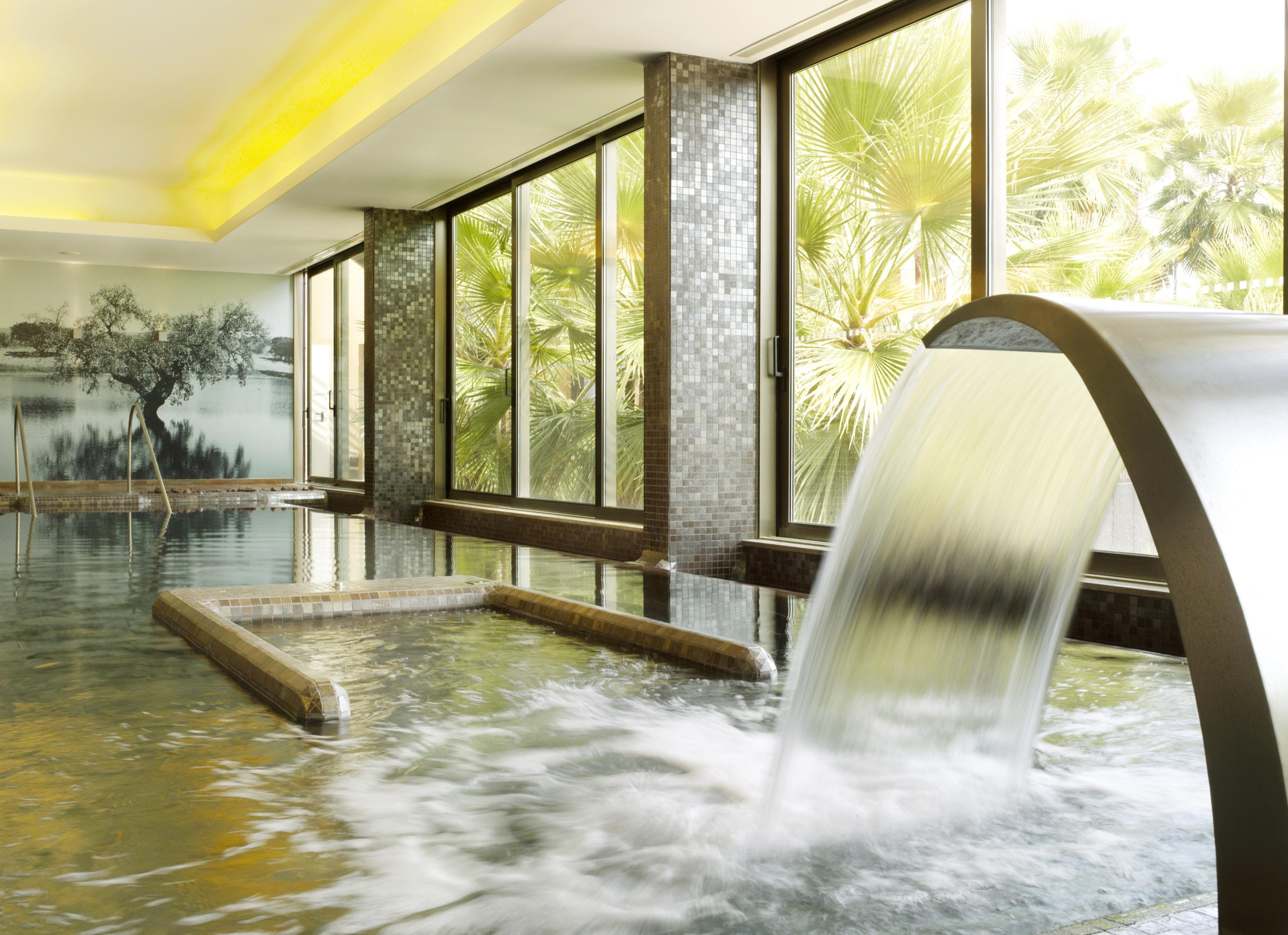 Ap Lago Montargil - Conference & Spa Ngoại thất bức ảnh The photo depicts a serene spa environment featuring a tranquil indoor pool area. There is a sleek, modern water feature that spills water gracefully into the pool. Large windows allow natural light to flood the space, showcasing views of lush greene
