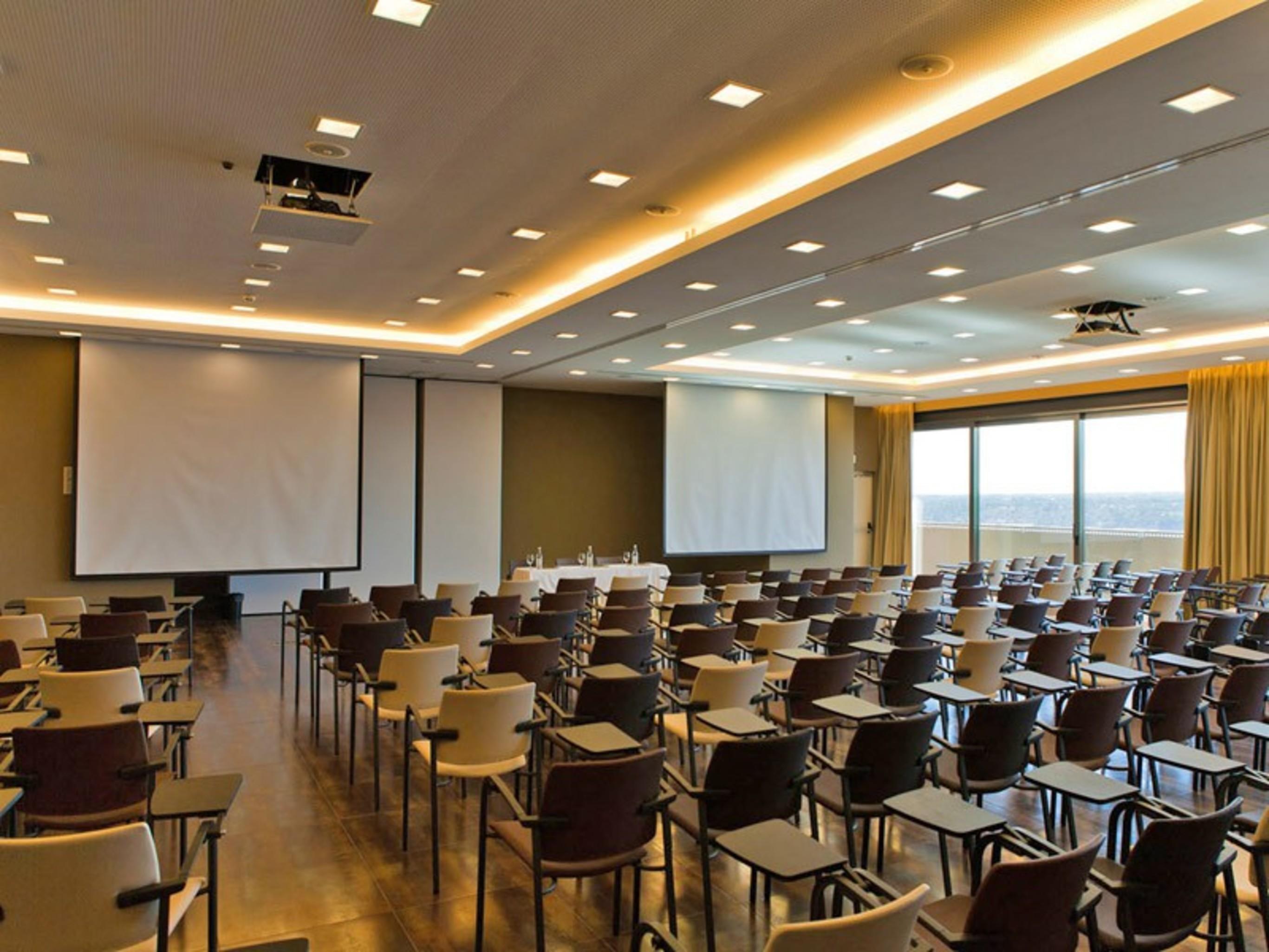 Ap Lago Montargil - Conference & Spa Ngoại thất bức ảnh The photo shows a large conference room set up for a presentation or meeting. There are multiple rows of chairs arranged in a semi-theater style, facing two large projection screens. The room has a modern design, with soft lighting and large windows 