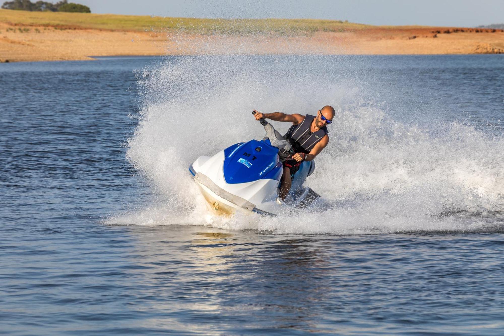 Ap Lago Montargil - Conference & Spa Ngoại thất bức ảnh The photo shows a person riding a jet ski over a body of water. The rider is wearing sunglasses and a life vest, leaning forward as the jet ski accelerates, creating a spray of water around them. The background features a natural landscape, likely a 