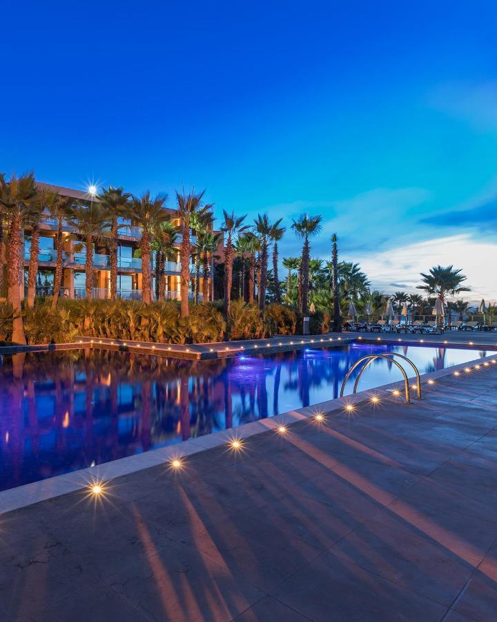 Ap Lago Montargil - Conference & Spa Ngoại thất bức ảnh The image shows a serene and inviting outdoor area with a large swimming pool that features a beautiful blue hue, likely illuminated by lights. Surrounding the pool are well-maintained palm trees and lush greenery, creating a tropical atmosphere. In 